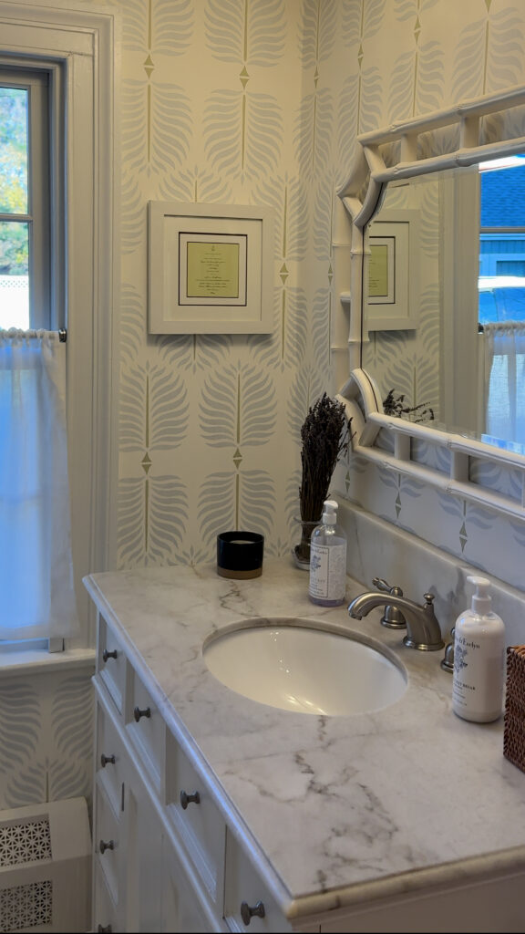 Bathroom remodeling by Omega Development in Westport CT. Bathroom sink with a marble countertop, framed mirror, and decorative items including soap and a vase.
