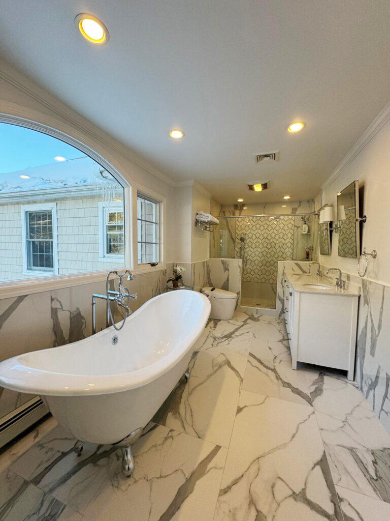 Bathroom remodeling in CT by Omega Development LLC. Modern bathroom with a freestanding bathtub, marble surfaces, a glass shower, and a white vanity.