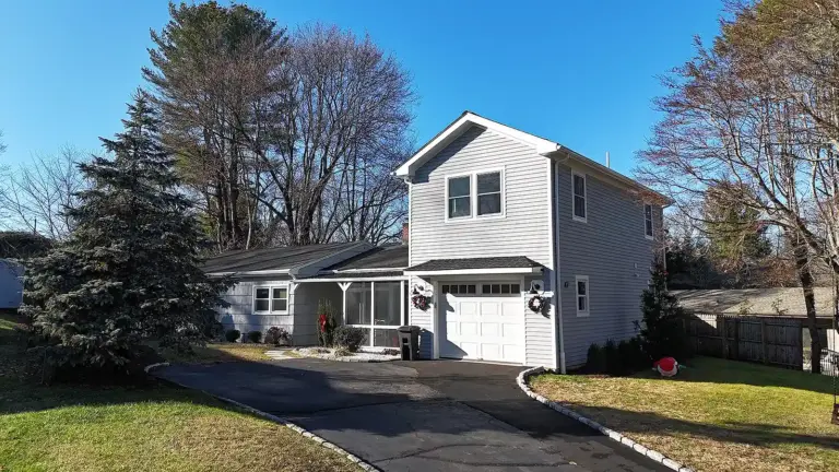 Driveway paving contractor in CT. Two‑story gray house with a garage, green lawn, and holiday decorations in the yard.