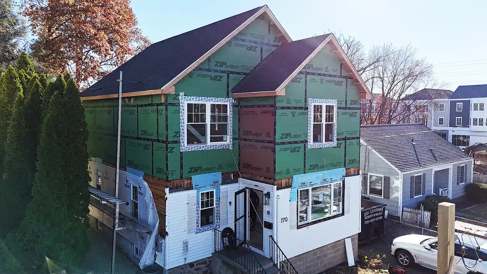 Home renovation and remodeling in Connecticut. House under renovation with new upper-level framing covered in green and red sheathing, windows installed, and construction materials around the yard.