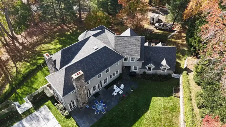 Roofing contractor in CT. Aerial view of a large house with a landscaped yard, patio furniture, and surrounding trees.